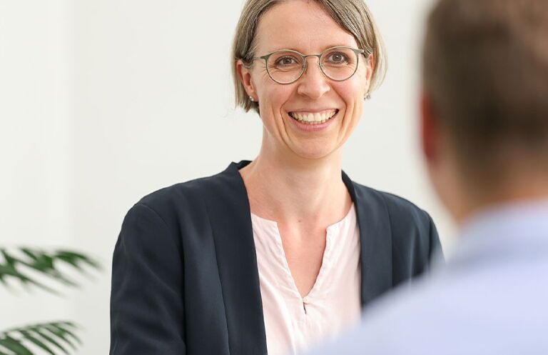 Beratungsgespräch zwischen einer Mitarbeiterin und einem Mitarbeiter in einem hellen Büro, Mitarbeiterin ist von Vorne zu sehen