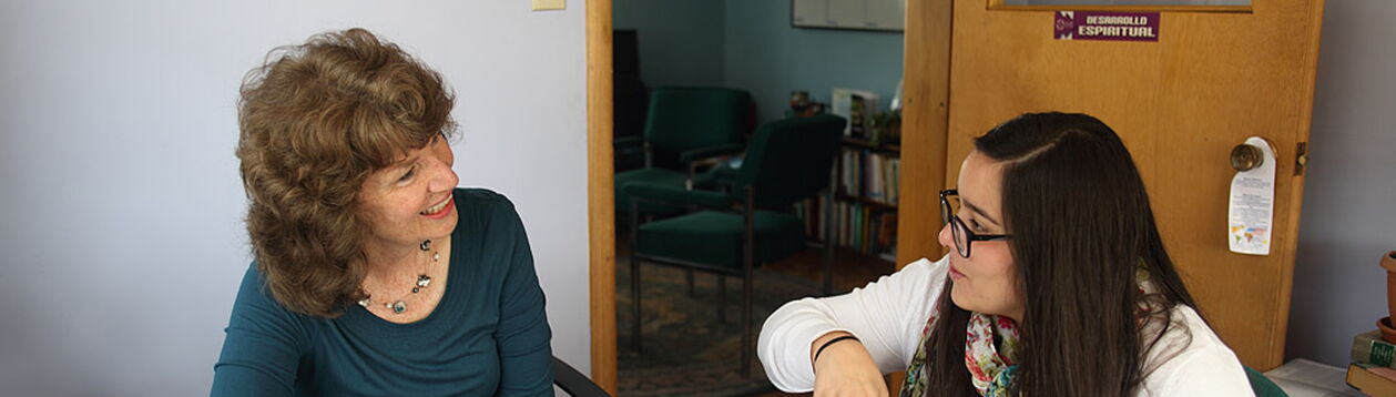 Esther Neufeld erklärt einer Frau etwas an einem Tisch mit offenen Büchern, lächelnd