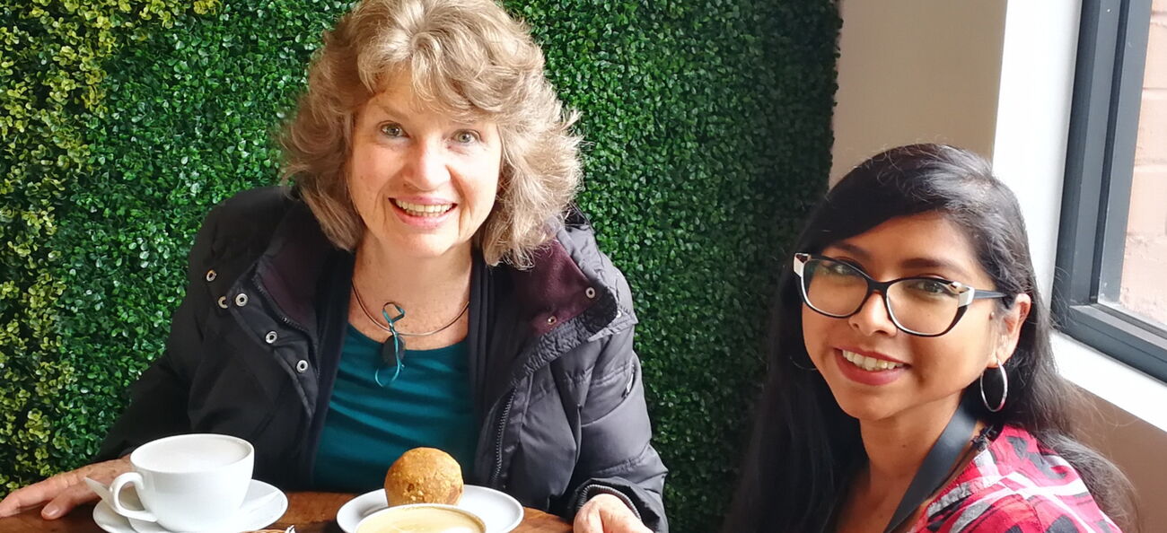 Esther Neufeld am Tisch beim Frühstück mit einer Frau, in die Kamera lächelnd