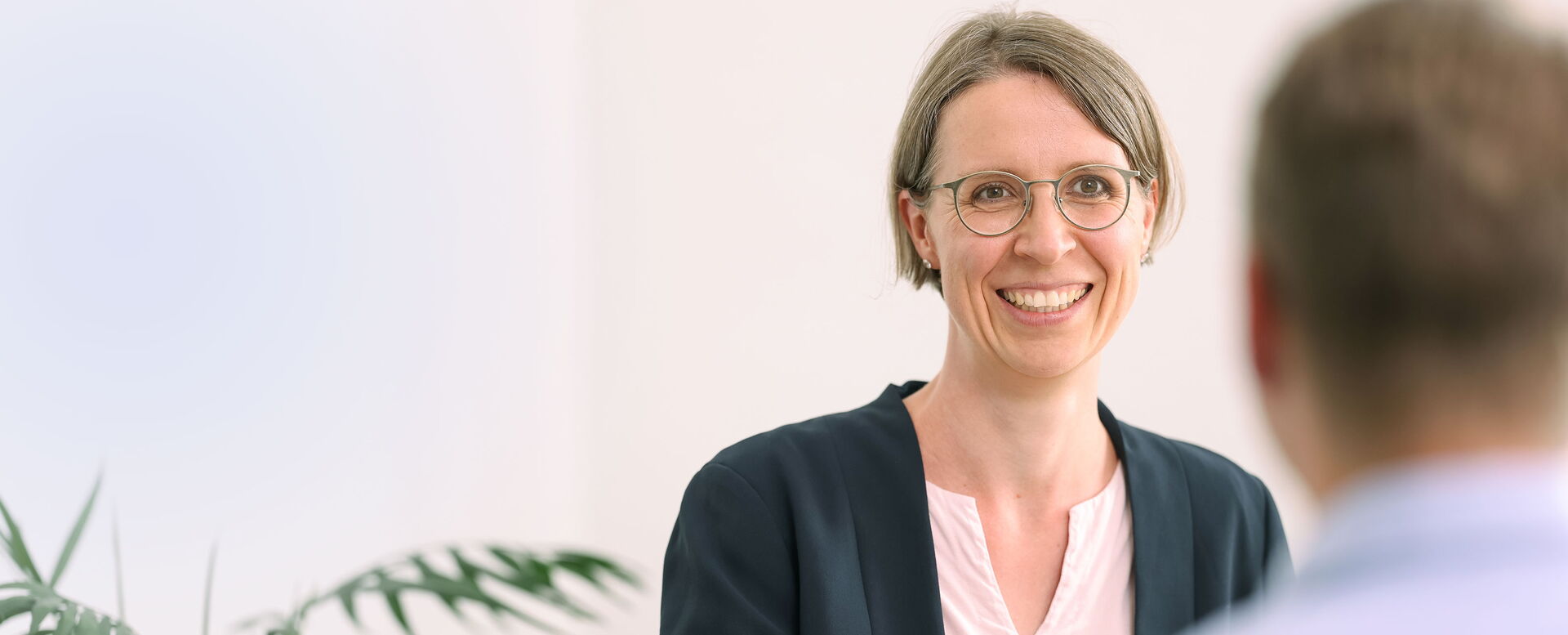 Beratungsgespräch zwischen einer Mitarbeiterin und einem Mitarbeiter in einem hellen Büro, Mitarbeiterin ist von Vorne zu sehen