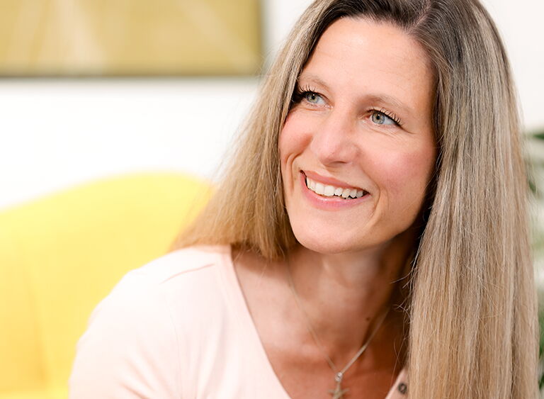 Lächelnde Frau im Gespräch, sitzt auf gelbem Stuhl in modernem, hellen Büro