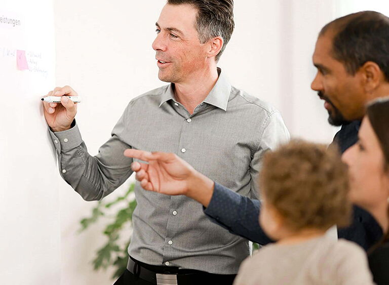 Beratungsgespräch zwischen einem Mitarbeiter und einer Familie an einem Whiteboard